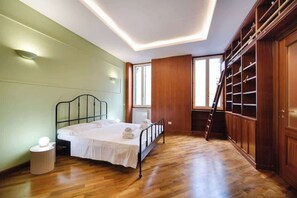 A bedroom with a bed, bedside lamp, wooden floor, built-in shelving, and a window. - BuddyRent - Dadada - Trevi - 8 ospiti (Roma)