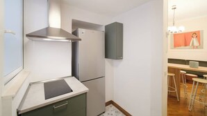 Eine kompakte Küche mit Einbauherd, Edelstahl-Dunstabzugshaube, einer Kühlschrank mit zwei Türen und einer Bar mit Hockern.