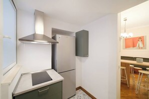 Cocina compacta con estufa integrada, extractor de acero inoxidable, refrigerador de dos puertas y una barra con taburetes.