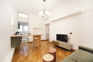 A modern living room with a wooden floor, a TV, a sofa, a dining area with stools, and a kitchen area. - BuddyRent - Dadada - Trevi - 8 ospiti (Roma)