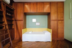 Een kleine kamer met een bed, een houten garderobe en een ladder.