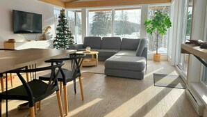 En moderne stue med træloft, en grå sofa, et spisebord med stole og et juletræ.