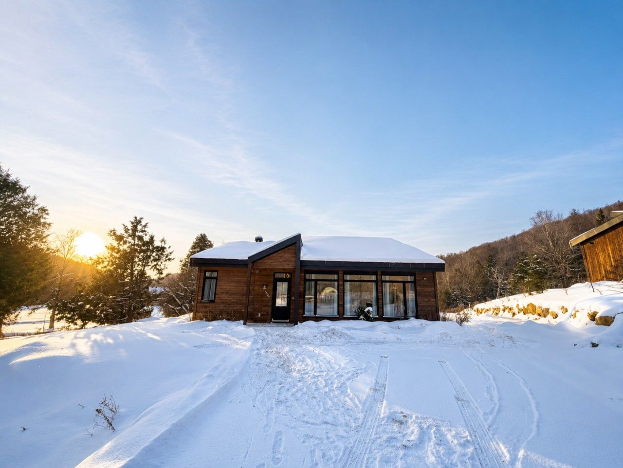 A wooden cabin with a snow-covered roof, large windows, and a clear sky.