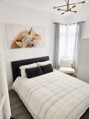 Une chambre à coucher avec un lit, une chaise, un tableau et une fenêtre avec des rideaux.
