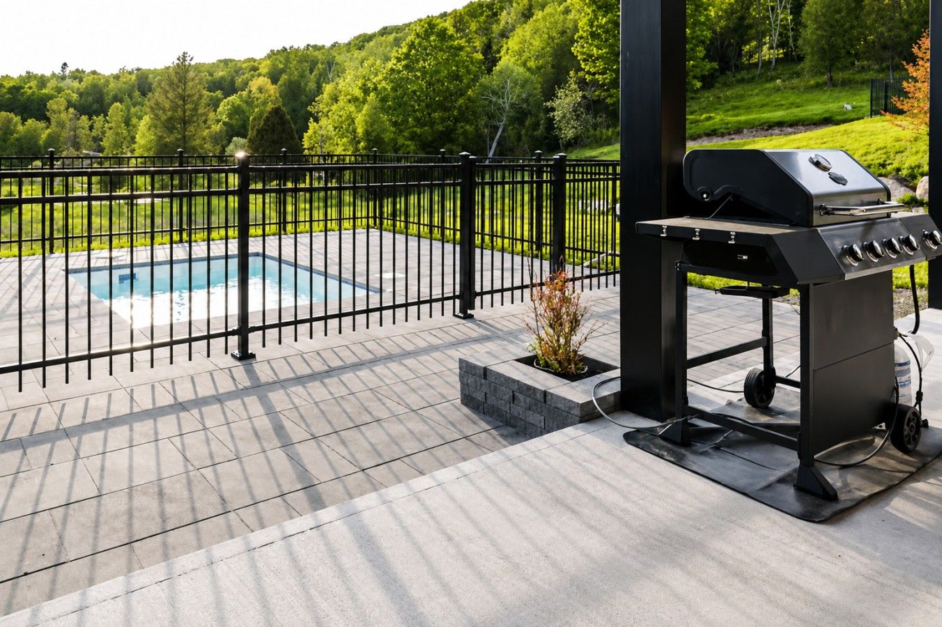 A patio with a grill, a pool, and a fenced area.