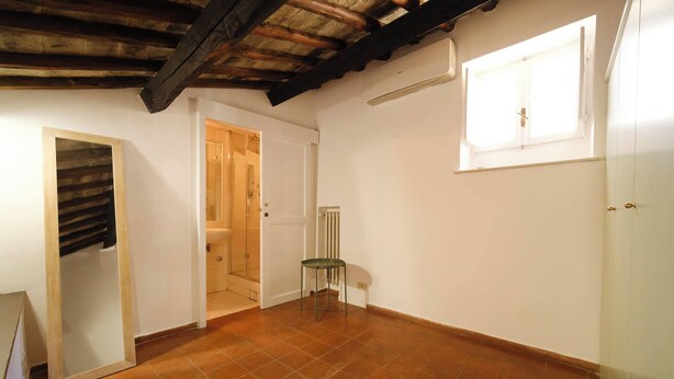 A room with a tiled floor, a door leading to a bathroom, a window with a blind, and a radiator. - BuddyRent - Borgo Pio's - San Pietro - 8 ospiti (Roma)