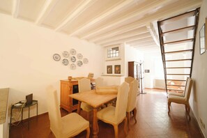 A dining area with a wooden table and chairs, a small side table with a laptop, and a radiator in the background.