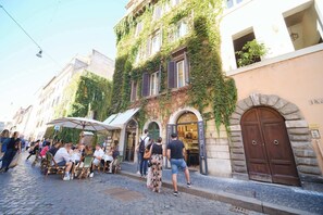 A cobblestone street with outdoor seating, a building with ivy-covered walls, and a stone archway.