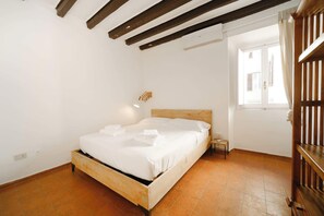 Ein Schlafzimmer mit einem hölzernen Bett, weißer Bettwäsche, einem Nachttisch, einer Wandleuchte und einem Fenster mit Vorhängen.