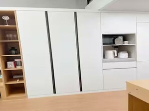 A modern kitchen with white cabinetry, a wooden shelf unit, and a countertop with kitchenware. - Ansan Modern Style Duplex - Kitchen & Washer (Ansan-si)