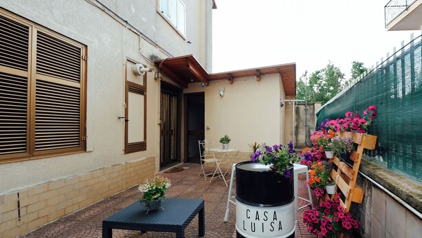 A courtyard with a black barrel labeled "CASA LUIS," a small table, and a bench.