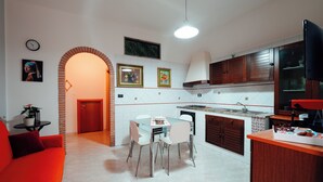 A modern kitchen with white tiles, wooden cabinets, and a dining area with a glass table and white chairs.