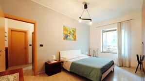 A bedroom with a bed, bedside tables, a window with curtains, a painting on the wall, and a door.