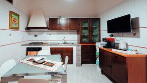 A compact kitchen with a dining area, a TV mounted above the counter, and a small island with a sink.