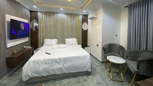 Une chambre d’hôtel moderne avec un grand lit, un téléviseur fixé au mur, une petite table ronde et un fauteuil confortable.