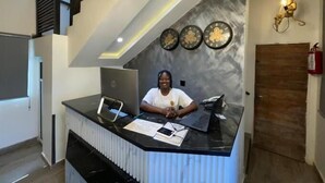Un comptoir d’accueil avec un ordinateur portable, un téléphone intelligent et quelques documents. Il y a trois horloges accrochées au mur, au-dessus du comptoir.