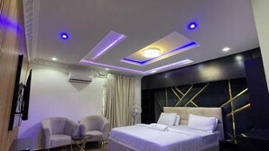 Une chambre d’hôtel moderne avec un grand lit, deux fauteuils, une petite table et un plafond doté d’un éclairage encastré et d’un puits de lumière.