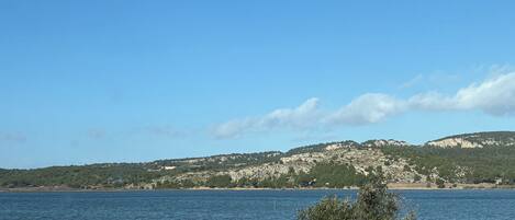 A coastal view with a clear sky, a body of water, and a rocky landscape in the distance.