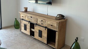 A room with a wooden cabinet, a mounted flat-screen TV, and two green vases on the floor. - Jules' keys (Gruissan)