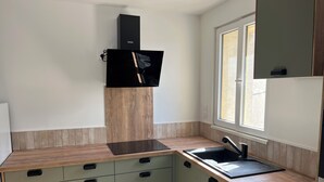 A modern kitchen with a wooden countertop, built-in cabinets, a black range hood, and a window providing natural light. - Jules' keys (Gruissan)