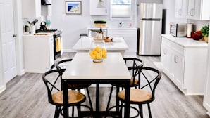 A modern kitchen with white cabinetry, a stainless steel refrigerator, and a dining area with a table and chairs. - Downtown - 2 bed, 2 bath (Raleigh)