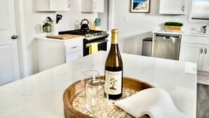 A kitchen with white cabinets, a stainless steel stove, and a wine bottle on a wooden tray. - Downtown - 2 bed, 2 bath (Raleigh)