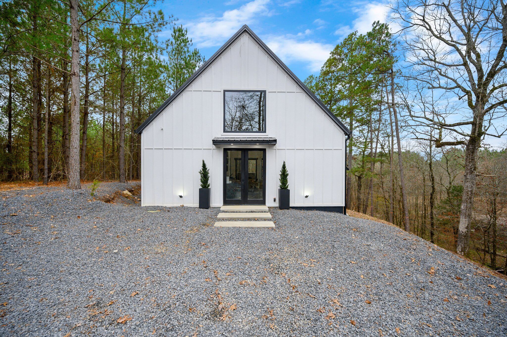A white building with a triangular roof, a large window, and two small potted plants at the entrance.