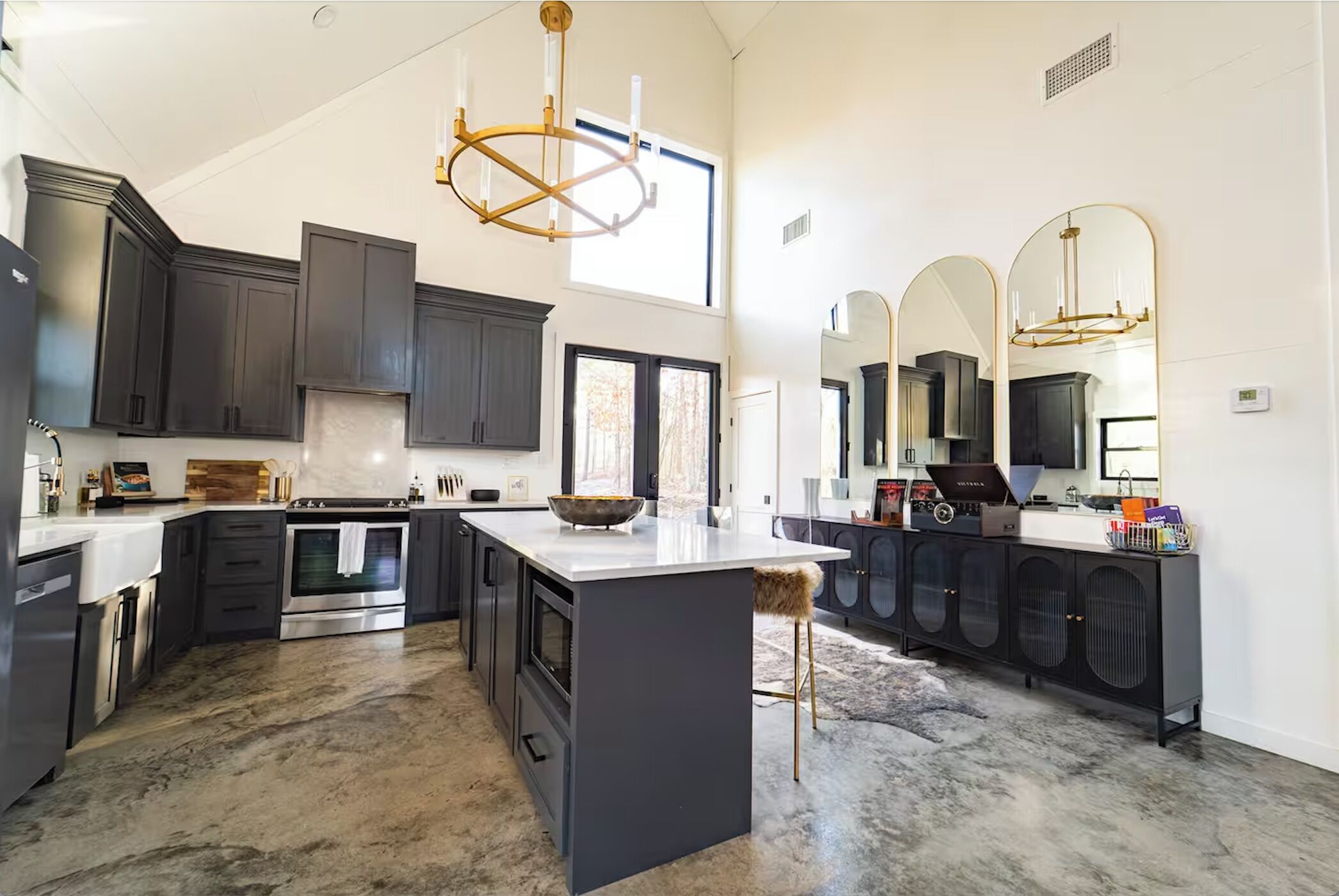 A modern kitchen with dark cabinetry, a large island, stainless steel appliances, and a chandelier.