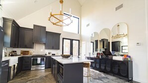 A modern kitchen with dark cabinetry, a large island, stainless steel appliances, and a chandelier. - Beautiful luxury romantic cabin: hot tub + outdoor swing + secluded+ creek (Broken Bow)