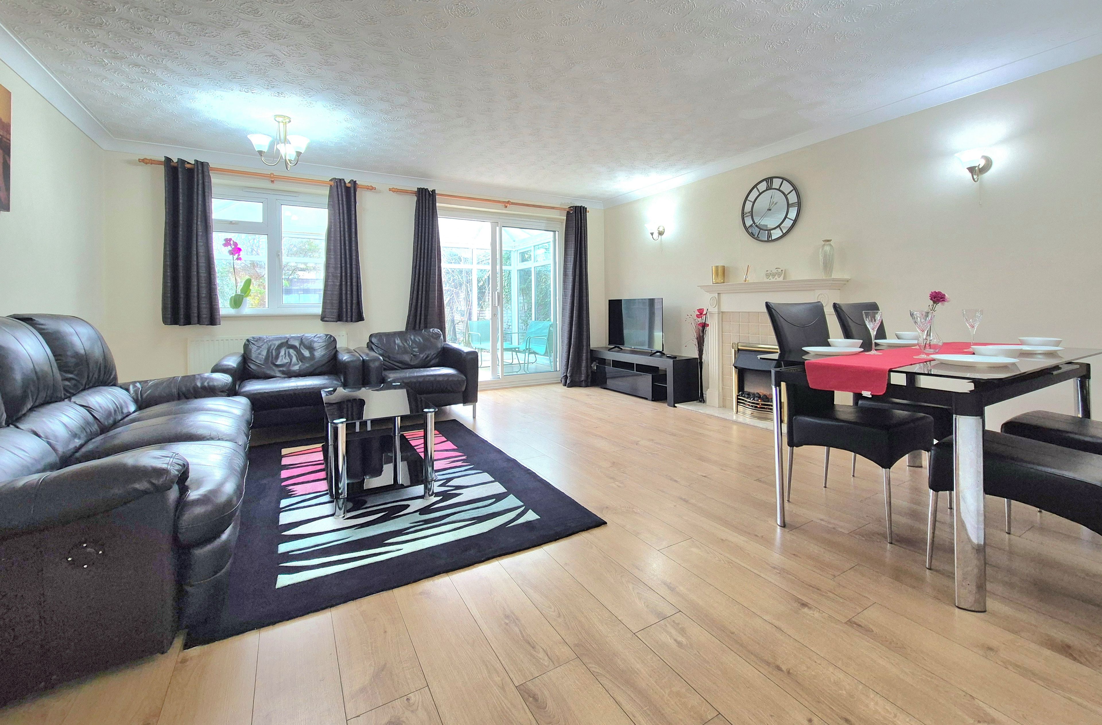 A living room with a sectional sofa, a dining table with chairs, a flat-screen TV, and a fireplace.