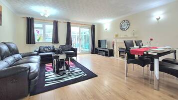 A living room with a sectional sofa, a dining table with chairs, a flat-screen TV, and a fireplace.
