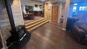 Amplia sala de estar con chimenea, piso de madera, mesa de comedor y sofá.
