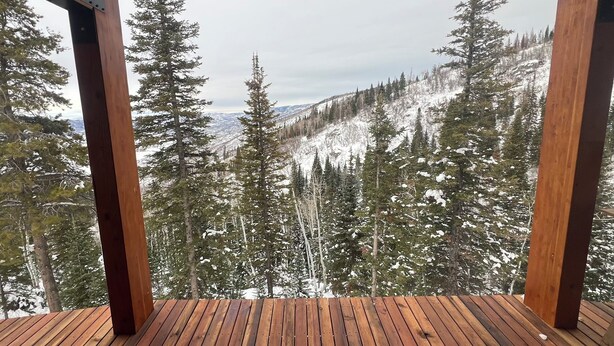 Una terraza de madera con vistas a árboles nevados y montañas distantes.