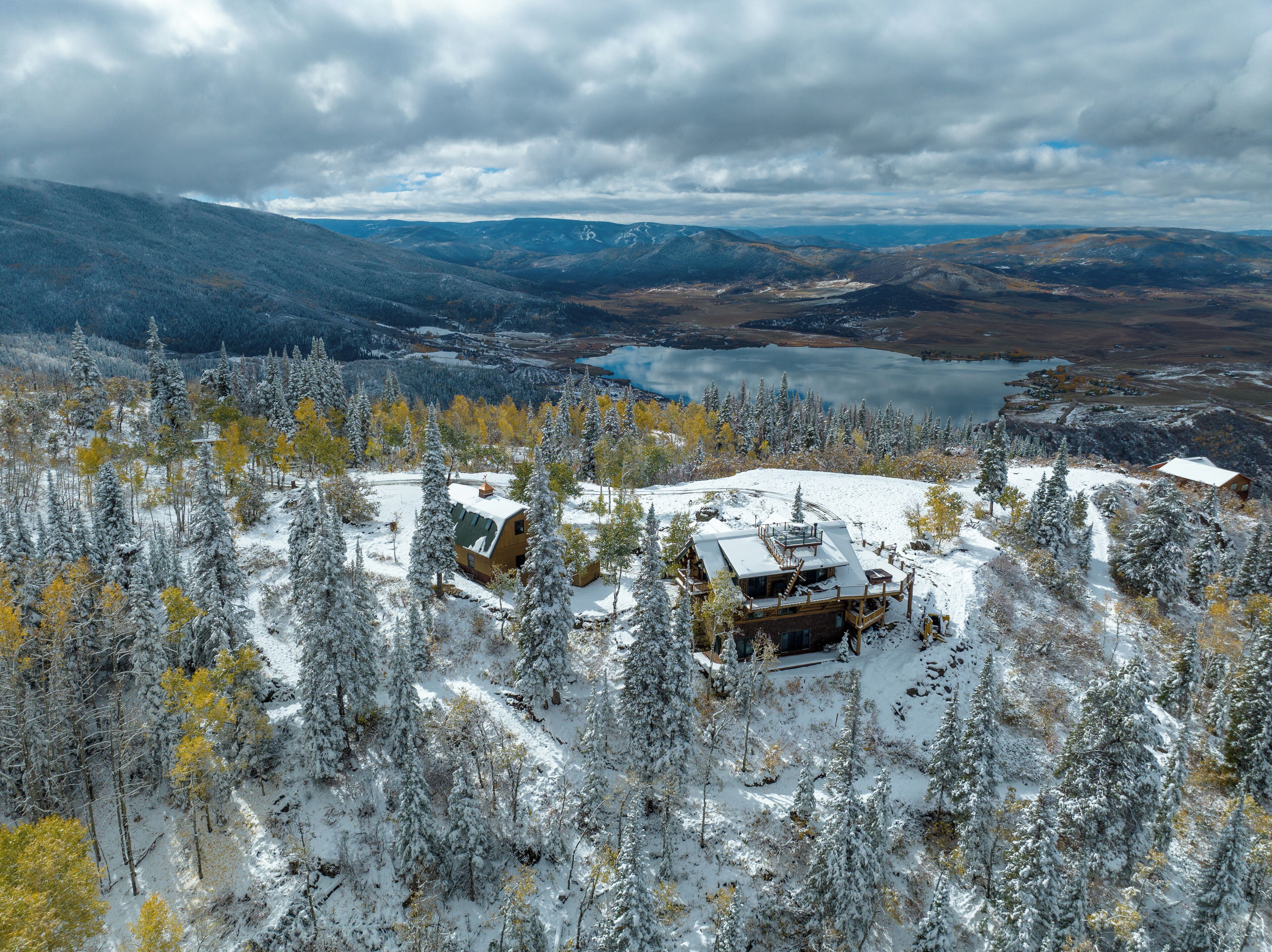 Una cabaña rodeada de árboles cubiertos de nieve y un lago al fondo.