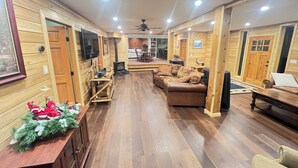 Acogedor interior de cabaña de madera con piso de madera, chimenea, sofá de cuero y comedor.