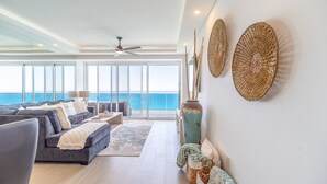Ein geräumiges Wohnzimmer mit großem Meerblick, Deckenventilator und dekorativer Wandgestaltung aus Webkunst.