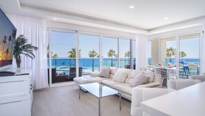 Un salon moderne avec une grande table en verre, un canapé et une vue sur l’océan grâce à de larges fenêtres.