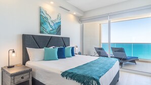 A modern bedroom with a large bed, a nightstand, a painting, and a balcony with chairs. - Splash Into Summer- Beachfront Condo @ the new Encantame Towers Resort (Puerto Peñasco)