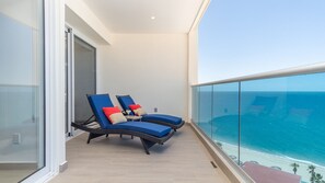 Un balcone con due poltrone, ringhiera in vetro e vista sull'oceano.