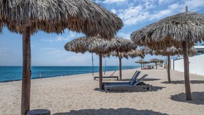 A beach with thatched umbrellas, lounge chairs, and a clear view of the sea.