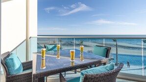 A balcony with a glass table and wicker chairs, overlooking a beach and ocean.