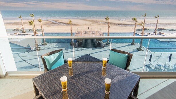 A balcony with a view of a beach and a pool area.