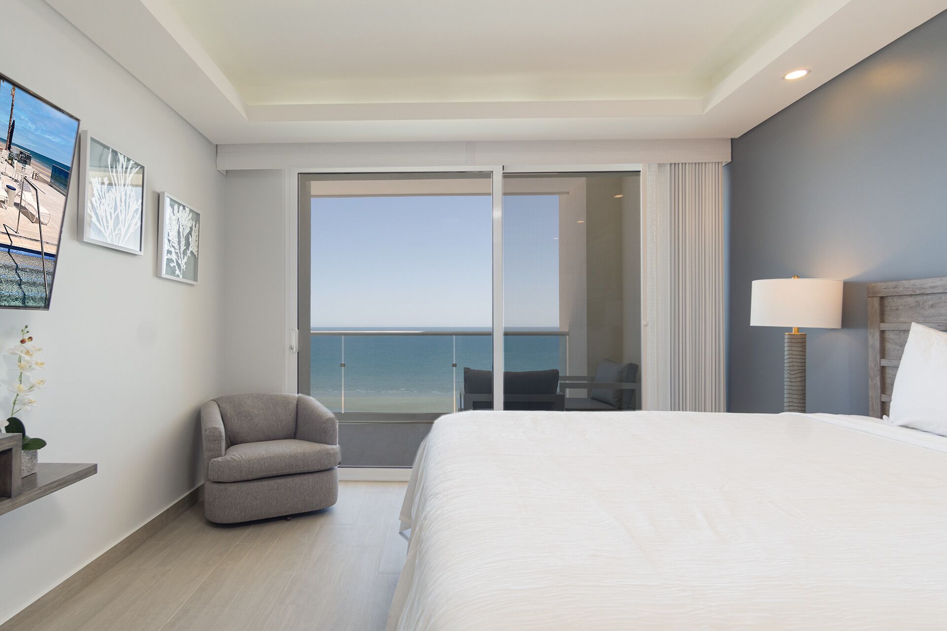A hotel room with a large bed, a chair, a desk, and a view of the ocean.