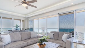 A spacious living room with a large grey sectional sofa, a wooden coffee table, and a ceiling fan. - Breathtaking 2 BR 2.5 Bath Corner Beach Front Condominium Encantame 505 (Puerto Peñasco)
