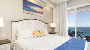 A hotel room with a large bed, a painting of a sunset, a balcony with a view of the sea, and a table with chairs. - Modish 2 BR Condo at Encantame Towers Velero 2204 (Puerto Peñasco)