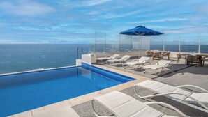 An infinity pool with lounge chairs and a table, overlooking the ocean. - Modish 2 BR Condo at Encantame Towers Velero 2204 (Puerto Peñasco)