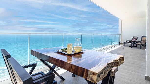A modern balcony with a wooden table, two chairs, and a glass railing overlooking the sea. - Modish 2 BR Condo at Encantame Towers Velero 2204 (Puerto Peñasco)