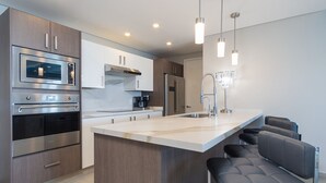 A modern kitchen with stainless steel appliances, a marble countertop, and a bar area with seating. - Modish 2 BR Condo at Encantame Towers Velero 2204 (Puerto Peñasco)
