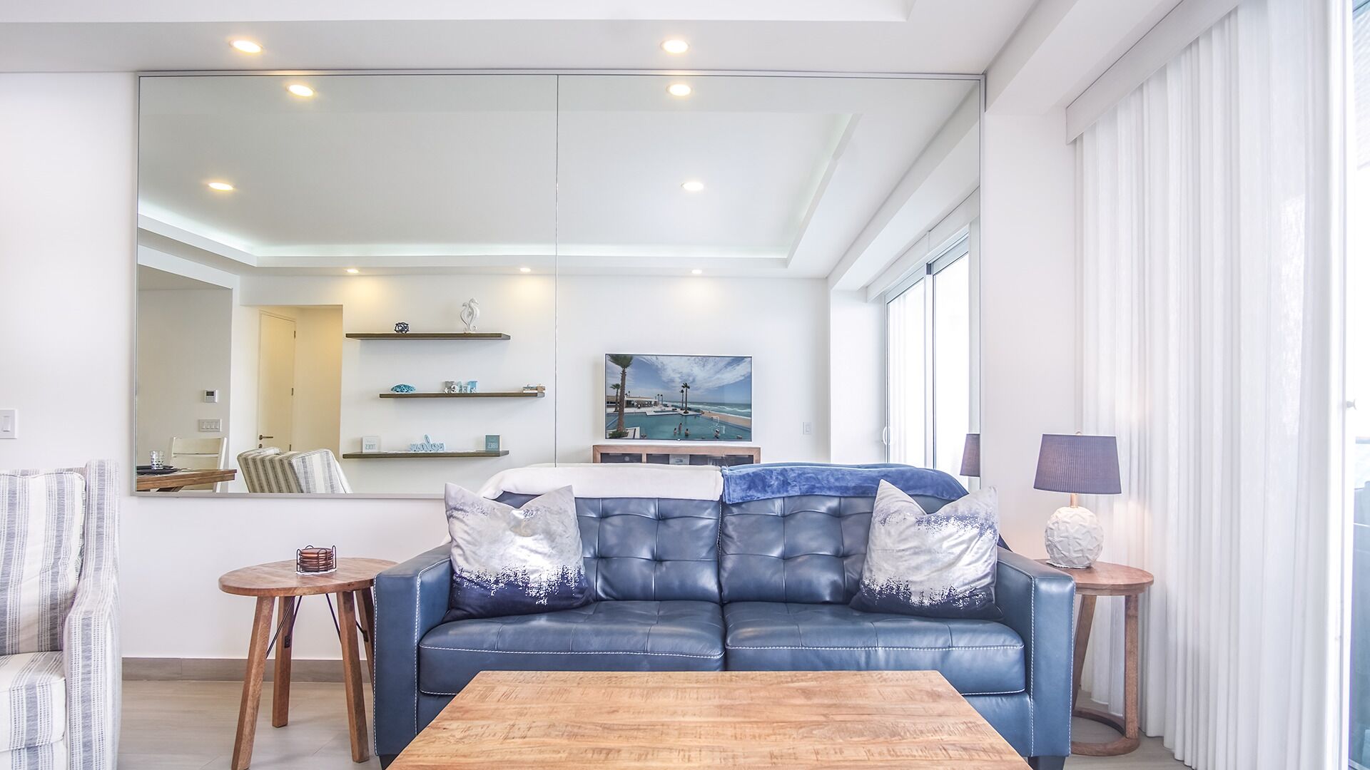 A modern living room with a blue leather sofa, a wooden coffee table, and a large mirror.