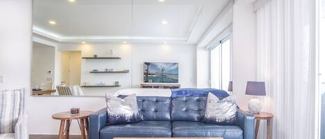 A modern living room with a blue leather sofa, a wooden coffee table, and a large mirror.